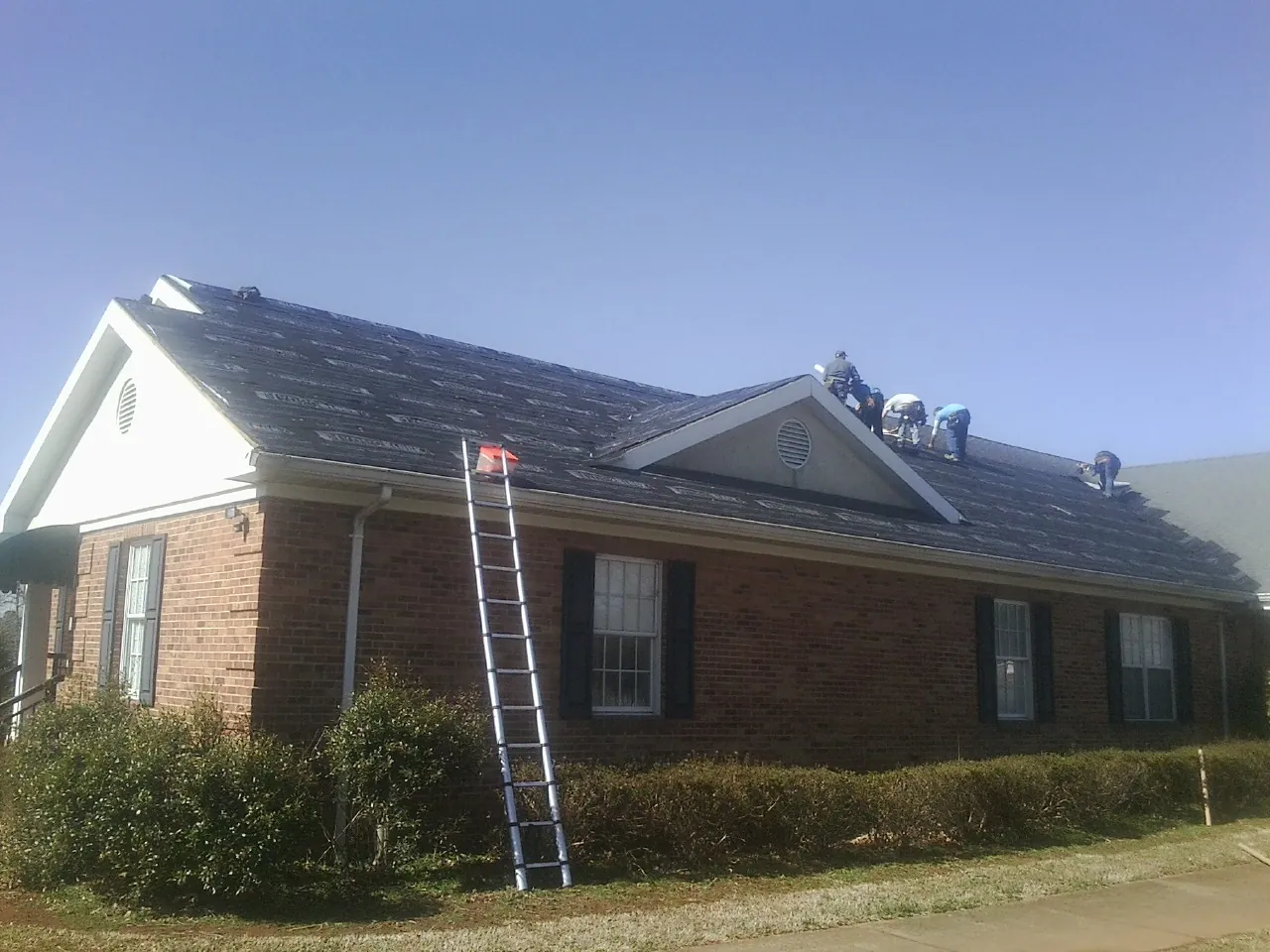 Crew tearing shingles off a brick ranch roof with a ladder set — Emergency Roof Repair work by our crew in Lansdale