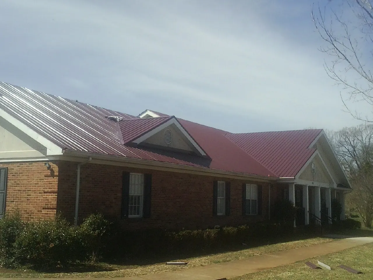 Red metal roof with gabled entries on a long brick building, from a Hail Damage Roof Repair job in Lansdale