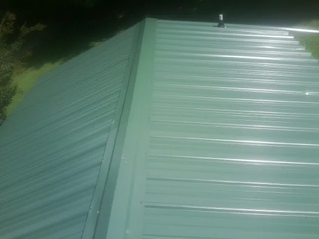New green metal panels meeting at the ridge of a roof — Flat Roof Repair work by our crew in Lansdale