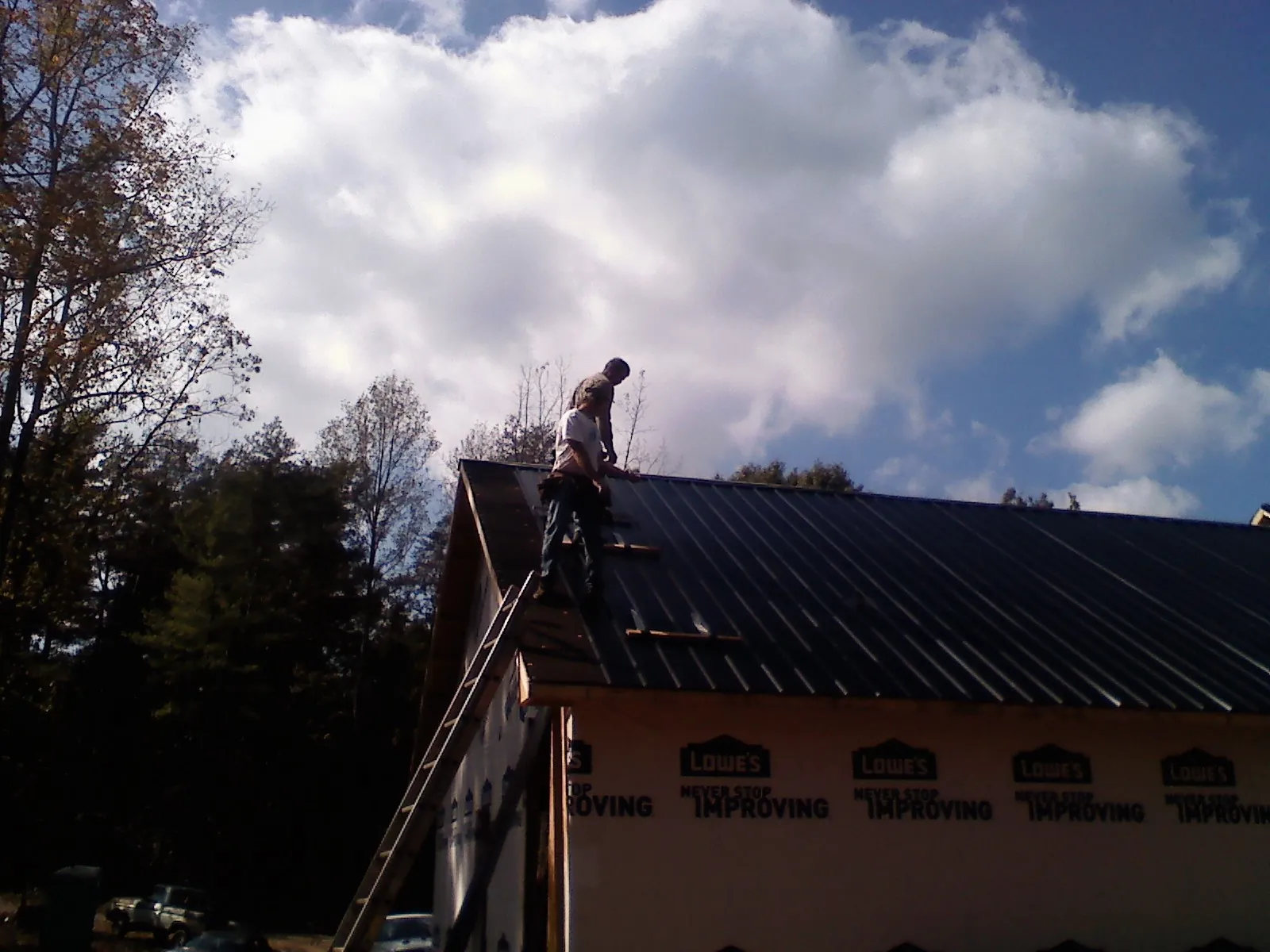 Roofer fastening dark metal panels high against a cloudy sky, from a Roof Inspection job in Lansdale