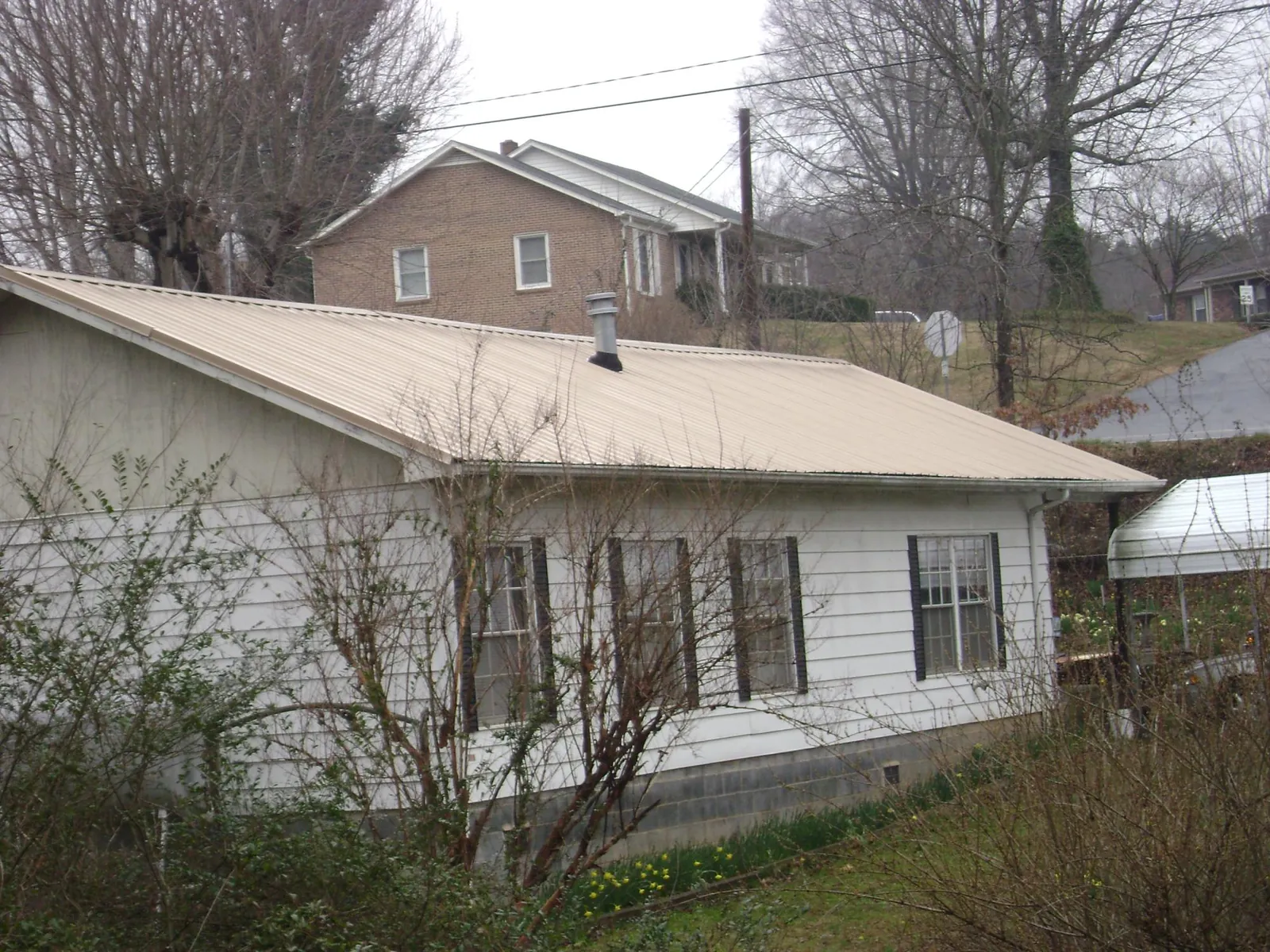 Tan metal roof on a white sided house set into a hillside — Commercial Roofing by Roofing Brothers in Lansdale